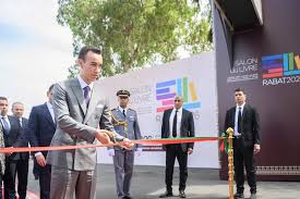 Man in a suit cuts a red ribbon at a formal ribbon-cutting ceremony, surrounded by officials with a branded backdrop in the background.