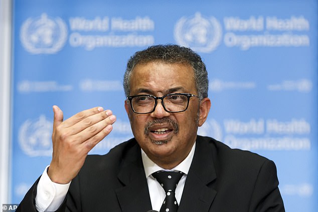 Man wearing glasses and a suit speaks at a World Health Organization briefing, gesturing with his right hand in front of a blue WHO backdrop.