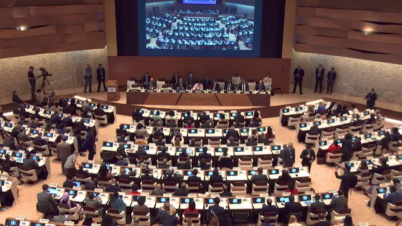 jjonn | MCG24 | موقع إلكتروني مغربي شامل متجدد على مدار الساعة Large international conference hall with delegates seated at curved desks facing a central stage and big screen projection above the podiums