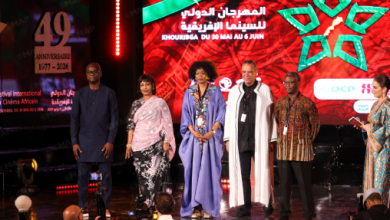 Six people stand on a lit stage during a film festival awards moment, with a red patterned backdrop and banners including a 49th anniversary sign on the left panel.
