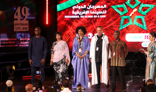 Six people stand on a lit stage during a film festival awards moment, with a red patterned backdrop and banners including a 49th anniversary sign on the left panel.