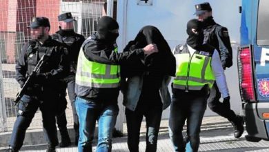 l89h0EFWQQVbN6raAA5B2MacbCiHpNJAZOWO8fVx | MCG24 | موقع إلكتروني مغربي شامل متجدد على مدار الساعة Masked police officers escort a hooded detainee toward a blue van during an arrest on a street edge with a visible reflective vest.