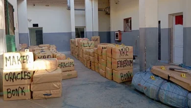 Indoor storage area with stacked brown boxes labeled with cryptocurrency names (XRP, Ethereum, Bitcoin, Maker, Oracle).