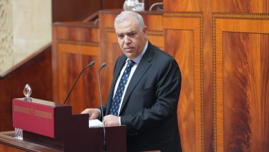 laftit-parlement | MCG24 | موقع إلكتروني مغربي شامل متجدد على مدار الساعة Man in a dark suit delivering a speech at a wooden podium with two microphones in a wood-paneled chamber.