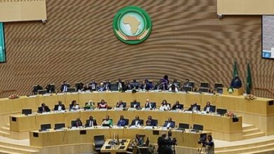 Africa Union emblem above a tiered semicircular council chamber where delegates sit around long desks in formal session.