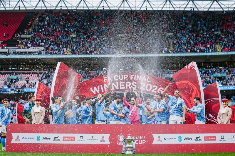 manchester-city-coupe | MCG24 | موقع إلكتروني مغربي شامل متجدد على مدار الساعة Team of players celebrates on stage with confetti and trophy after winning the Emirate Cup 2026 final in a packed stadium, banner reads 'Winners 2026'.