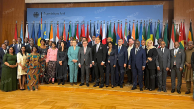Large group of dignitaries and international delegates posing on a stage with rows of national flags in the background, during a formal ceremony.