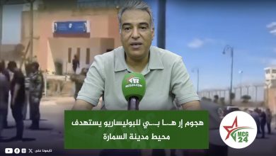 News anchor speaks into a green MCG24 microphone with an Arabic headline banner on a city backdrop behind him.