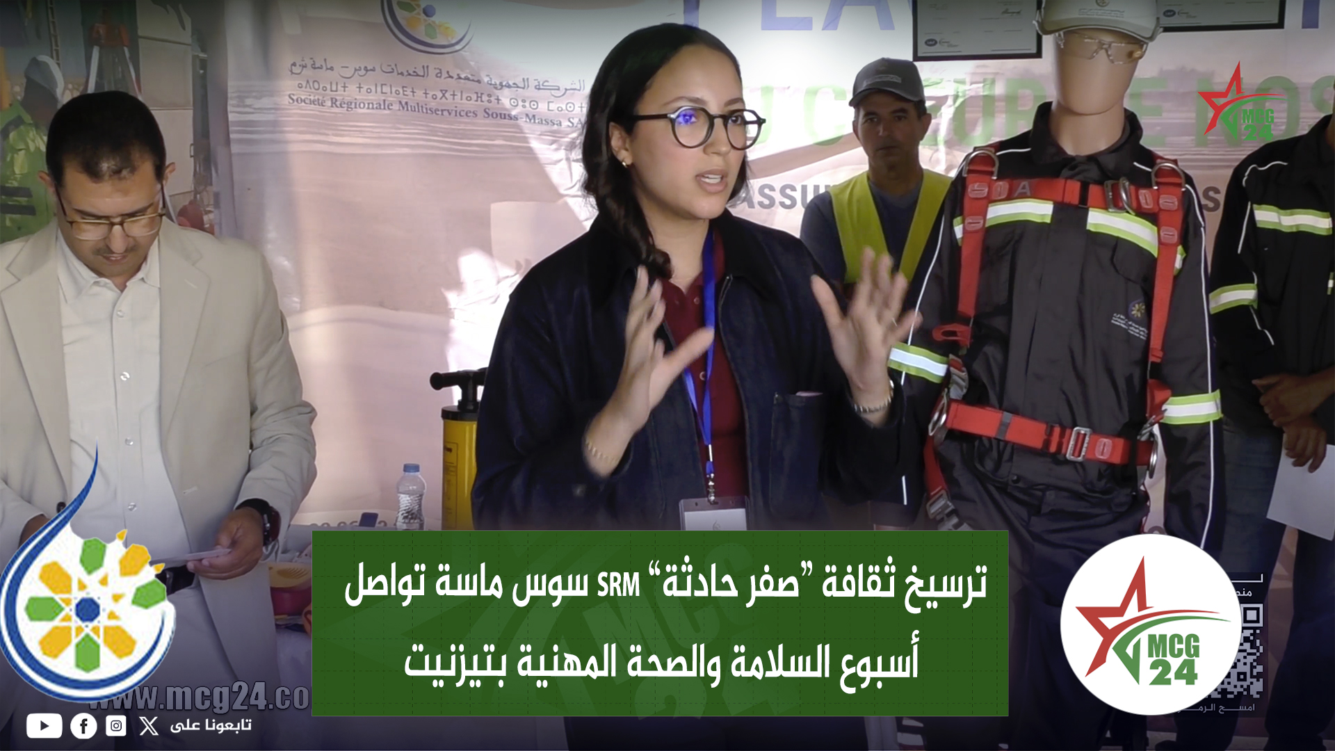 Woman with glasses speaks at a conference, flanked by a man in a suit and a rescue worker in safety gear beside her, with an Arabic banner behind.