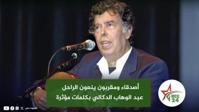 Man singing at a microphone on stage, wearing a dark suit; a green Arabic headline banner covers the lower part of the image.