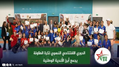 Group of students and adults posing with certificates at a sports award ceremony in a gymnasium hall.