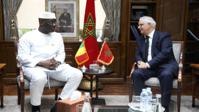 pic91223 | MCG24 | موقع إلكتروني مغربي شامل متجدد على مدار الساعة Two men in a formal office sit facing each other and discuss, with Moroccan flags between them and a framed portrait behind.