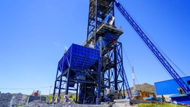 Heavy mining crane with a blue hopper elevated on a steel framework at a quarry site, with a long conveyor arm nearby