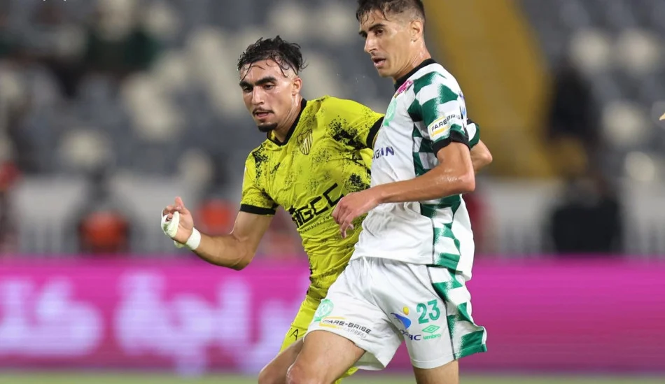 Two soccer players contest the ball during a match, one in a yellow kit and the other in a white-and-green striped kit, running side by side on the field.