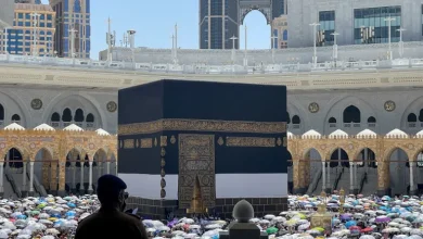 reuters_68469af2-1749457650 | MCG24 | موقع إلكتروني مغربي شامل متجدد على مدار الساعة Worshippers encircle the Kaaba at Masjid al-Haram, Mecca, with a silhouetted man in the foreground and colorful umbrellas in the courtyard.