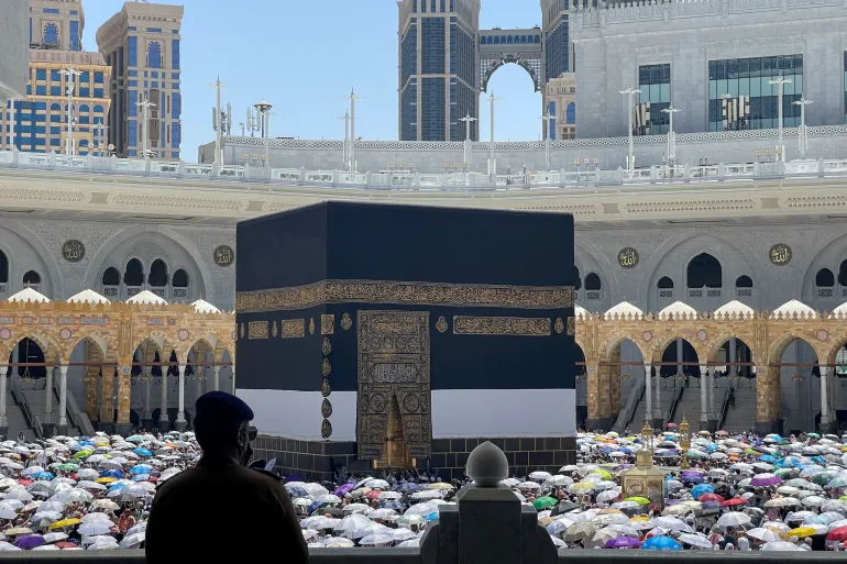 Worshippers encircle the Kaaba at Masjid al-Haram, Mecca, with a silhouetted man in the foreground and colorful umbrellas in the courtyard.