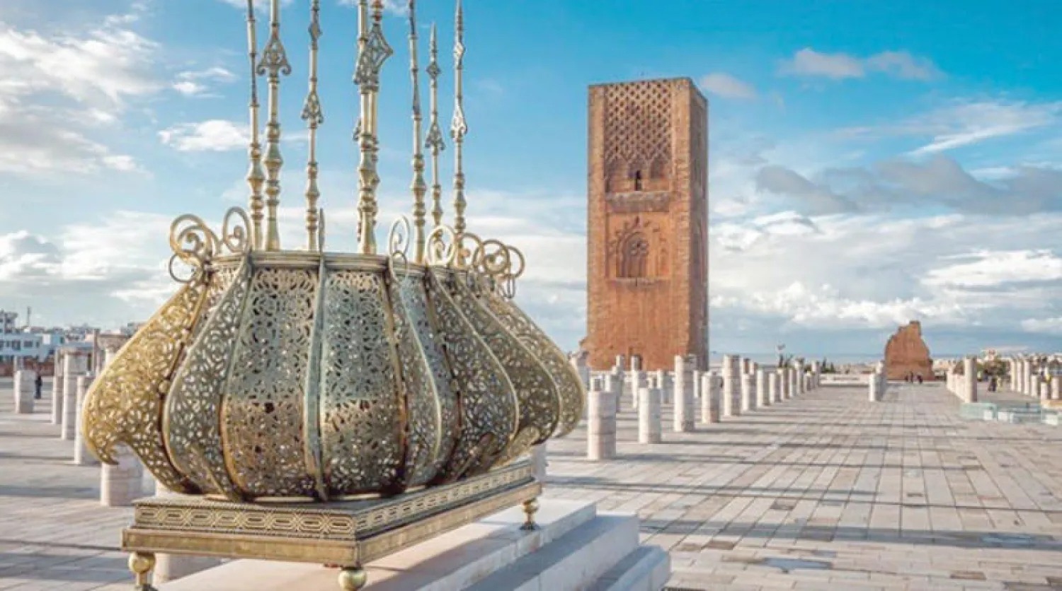 Ornate metal crown sculpture on a pedestal in a wide, tiled plaza, with a tall brick tower in the background.