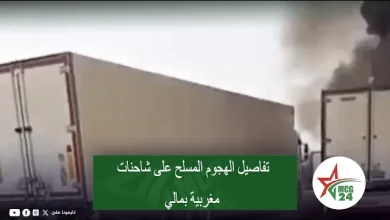 Two large trucks on a highway with dark smoke rising in the background; green Arabic caption banner about an armed attack on Moroccan trucks in Mali, with an MCG24 logo in the bottom right.