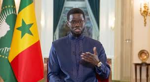 téléchargement | MCG24 | موقع إلكتروني مغربي شامل متجدد على مدار الساعة Man wearing blue traditional attire sits and speaks in a formal room, with the Senegal flag visible in the background.