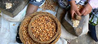 Basket of peanuts in a woven bowl beside a stone mortar and pestle, showing traditional peanut processing by hand in a market setting.