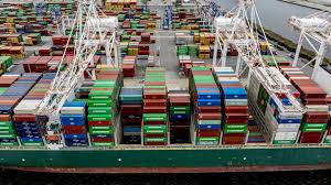 Aerial view of a cargo ship at port with rows of colorful shipping containers and large gantry cranes overhead