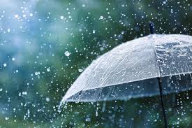 Clear umbrella tilted in a heavy rain shower, with raindrops splashing around it.