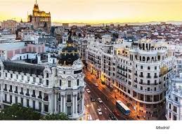 Aerial view of Madrid's historic center at sunset, featuring ornate white façades and a busy, lighted street below.