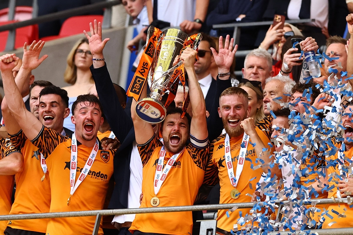 téléchargement 4 | MCG24 | موقع إلكتروني مغربي شامل متجدد على مدار الساعة Football team in orange jerseys celebrating with a large trophy raised above their heads, gold medals around their necks, confetti in blue and white.