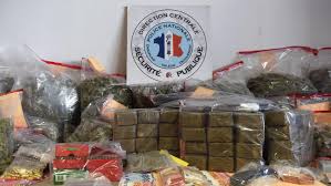 215154848 | MCG24 | موقع إلكتروني مغربي شامل متجدد على مدار الساعة Police drug bust display: stacked brick-like packs and bags of suspected drugs on a table with a police emblem in the background.