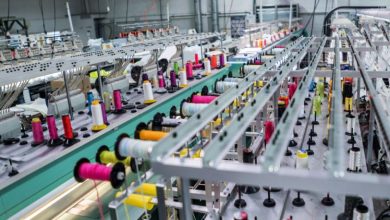 Industrial textile loom with rows of colorful thread spools along a conveyor system and threading hardware.