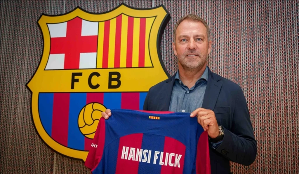 A man in a blue blazer holds up a blue-and-red FC Barcelona jersey in front of a large FC Barcelona shield.
