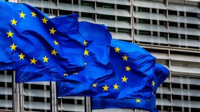 European Union flag waving against a glass-fronted office building in the wind.