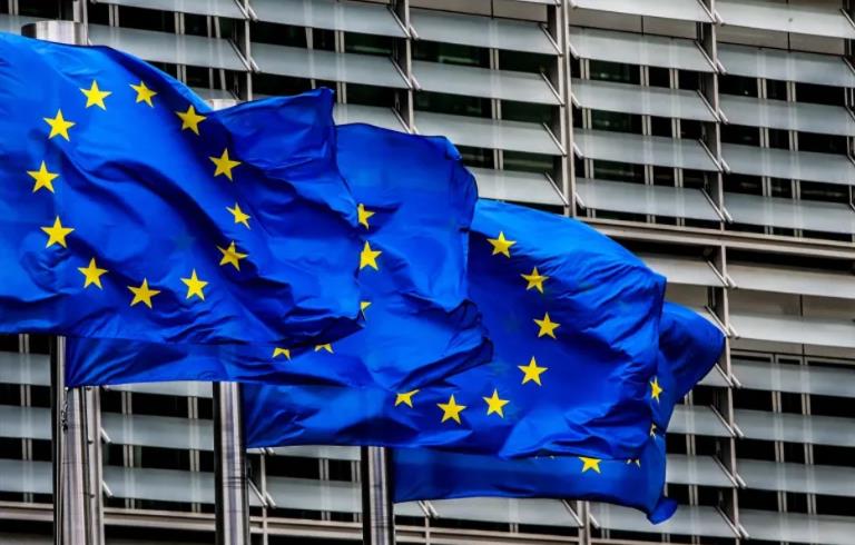 European Union flag waving against a glass-fronted office building in the wind.