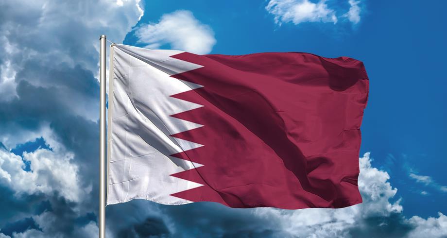 Qatar's flag waving in the wind against a blue sky.