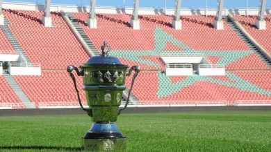 Polished trophy on a green soccer field with red stadium seats and a large turquoise star design in the background.
