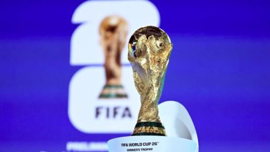 Golden FIFA World Cup trophy on a white pedestal against a blue backdrop, foreground in sharp focus.