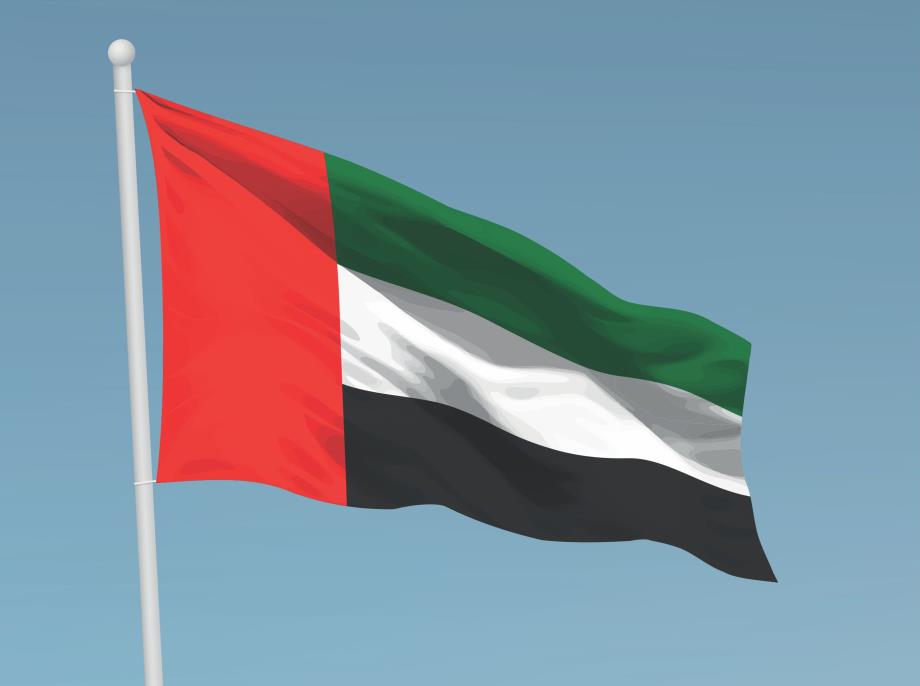 United Arab Emirates flag waving on a flagpole against a clear blue sky.