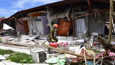 Rescue worker wearing a helmet searches through collapsed rubble of a damaged house after a disaster.
