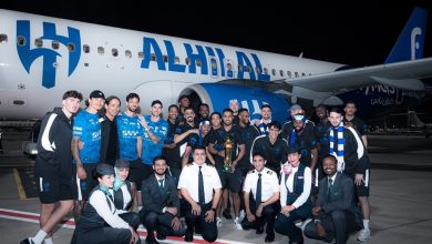 Group of airline crew and athletes posing with a trophy beside a blue-and-white airplane at night on the tarmac.