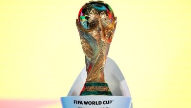 Gold FIFA World Cup original trophy with colorful reflections, set against a pale yellow background.