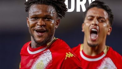 Two footballers in red kits celebrate a victory; the front player smiles at the camera while another teammate shouts in the background, with 'VICTORY' visible above.