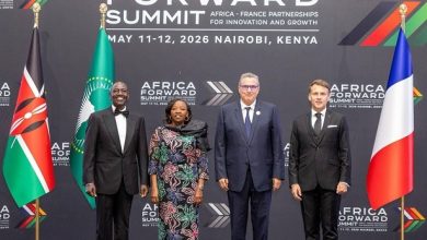 Four professionally dressed individuals posing on a stage at the Africa Forward Summit backdrop, with Kenyan and French flags visible.