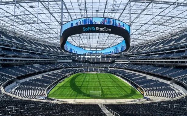 vis_0512202612570396 | MCG24 | موقع إلكتروني مغربي شامل متجدد على مدار الساعة Inside SoFi Stadium, a circular video board hangs above a bright green field with empty dark seats surrounding it.