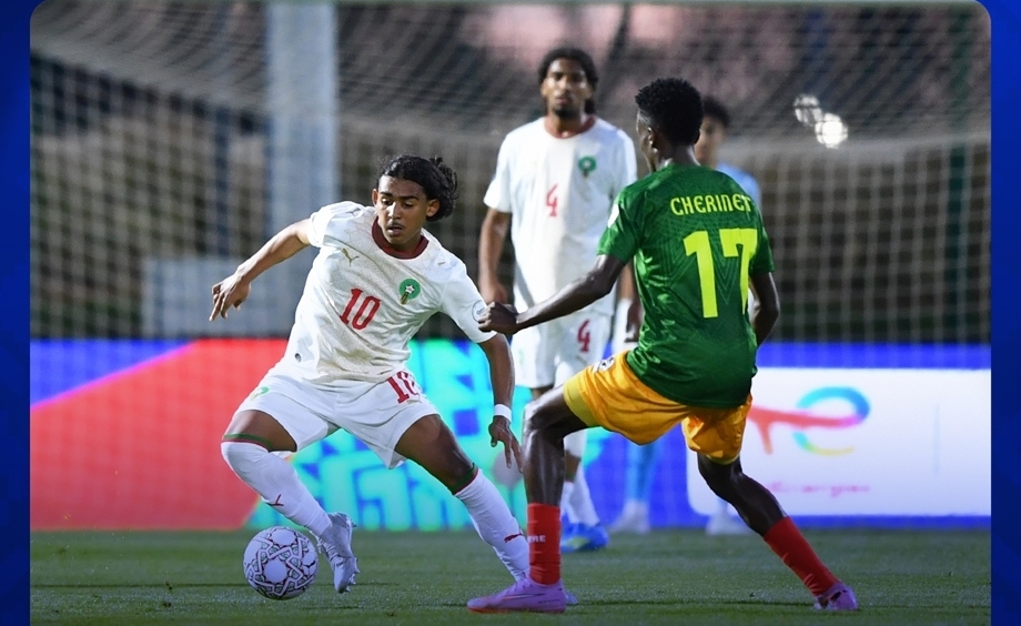 vis_0516202622113906 | MCG24 | موقع إلكتروني مغربي شامل متجدد على مدار الساعة Soccer players in white and green contest the ball on a well-lit field; white #10 dribbles against green #17 Cherinet near the goal area.