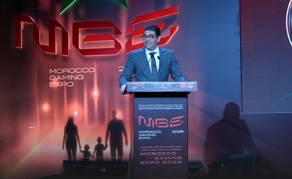 vis_0521202600131195 | MCG24 | موقع إلكتروني مغربي شامل متجدد على مدار الساعة Man in a suit delivering a speech at a lectern on stage at the Morocco Gaming Expo 2028.