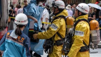 5154548484 | MCG24 | موقع إلكتروني مغربي شامل متجدد على مدار الساعة Firefighters in yellow suits and helmets assist a person in a blue protective gown on a crowded street.