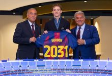 Three men in suits present a blue jersey labeled Gordon and 2031, standing behind a scale model stadium.