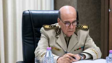 الجنرال حسان | MCG24 | موقع إلكتروني مغربي شامل متجدد على مدار الساعة Senior military officer in a beige dress uniform, writing at a desk with a pen, wearing glasses and a watch.