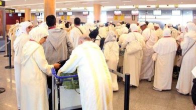 الحج | MCG24 | موقع إلكتروني مغربي شامل متجدد على مدار الساعة Crowd of travelers in white traditional robes lined up at airport check-in counters.