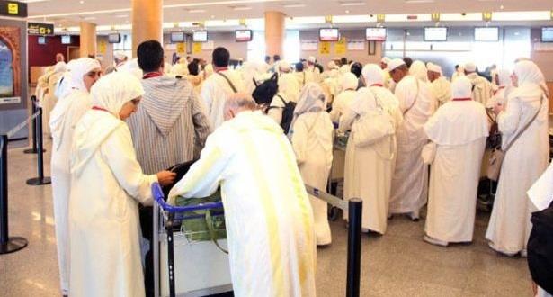 Crowd of travelers in white traditional robes lined up at airport check-in counters.